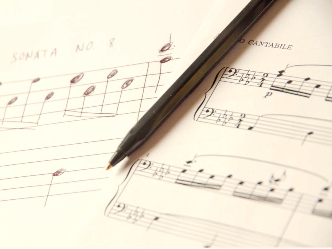 Handwritten and printed sheet music with a pen